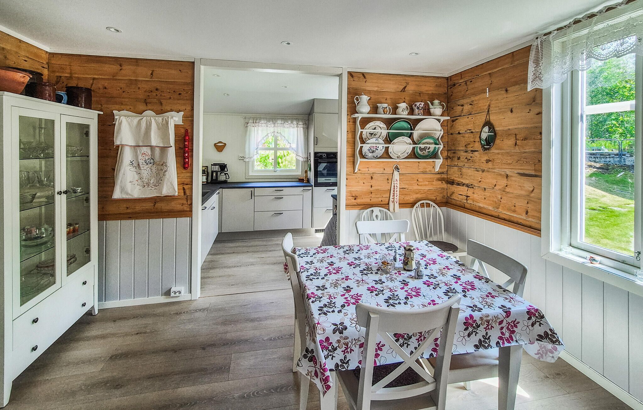 Una cocina acogedora con paredes de madera, una mesa de comedor con mantel floral y vistas al jardín.