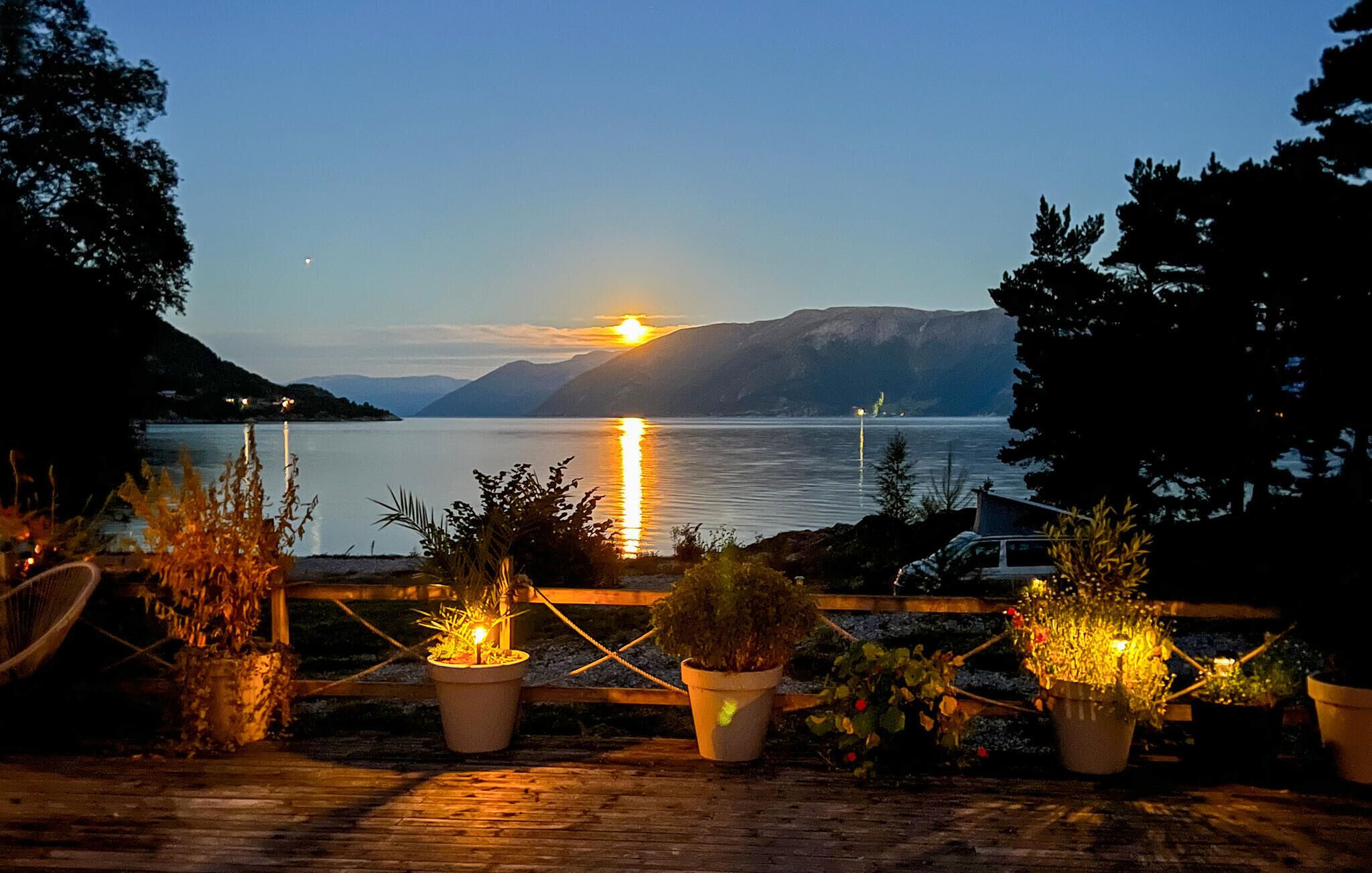 Vista para o lago com um pôr do sol, plantas em vasos e um deck de madeira.