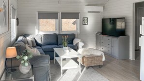 A cozy living room with a grey sofa, a white coffee table, a wicker chair, and a TV on a cabinet.