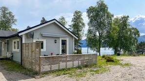 A small cabin with a porch, a covered deck, and a view of a lake and mountains.