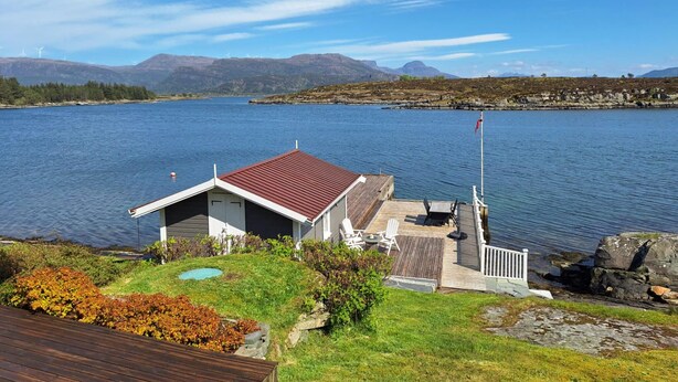 A lakeside cabin with a red roof, a deck, and a small pool. - Cozy home in Florø with WiFi (Florø)