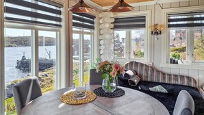 A dining area with a round table, chairs, and a bench. There are large windows with blinds, a view of a body of water, and a decorative wall with spherical elements. - Cozy home in Florø with WiFi (Florø)