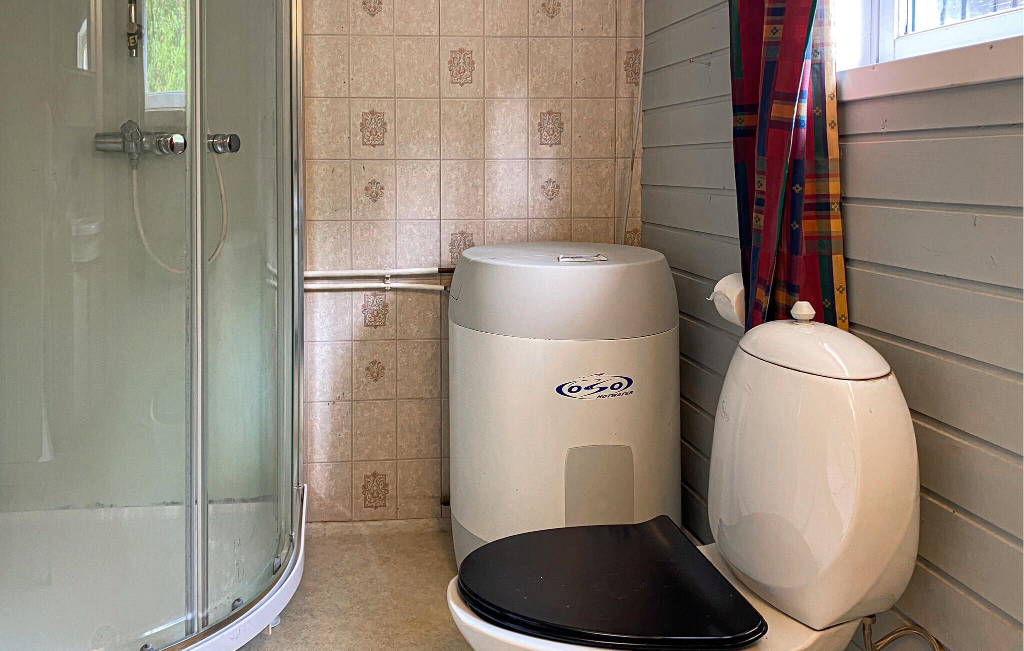 A bathroom with a glass shower enclosure, a toilet with a black seat, and a white hot water heater.