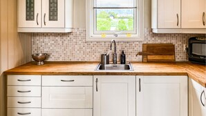 Una cocina con encimera de madera, pileta de acero inoxidable y muebles de color blanco.