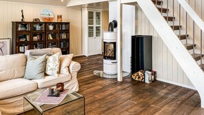 Una sala de estar con un sofá color beige, una mesa de centro de vidrio, una chimenea y una escalera.