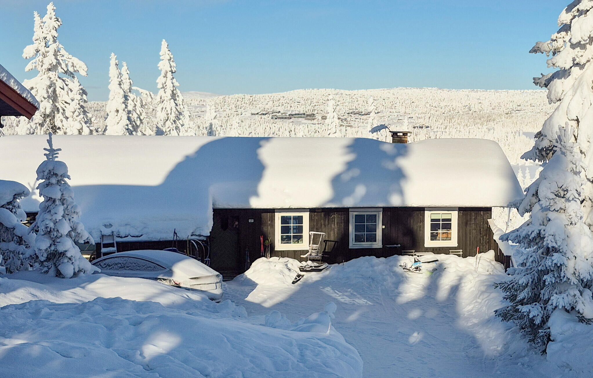 A snow-covered house with a garage, surrounded by snow-laden trees and a clear sky.