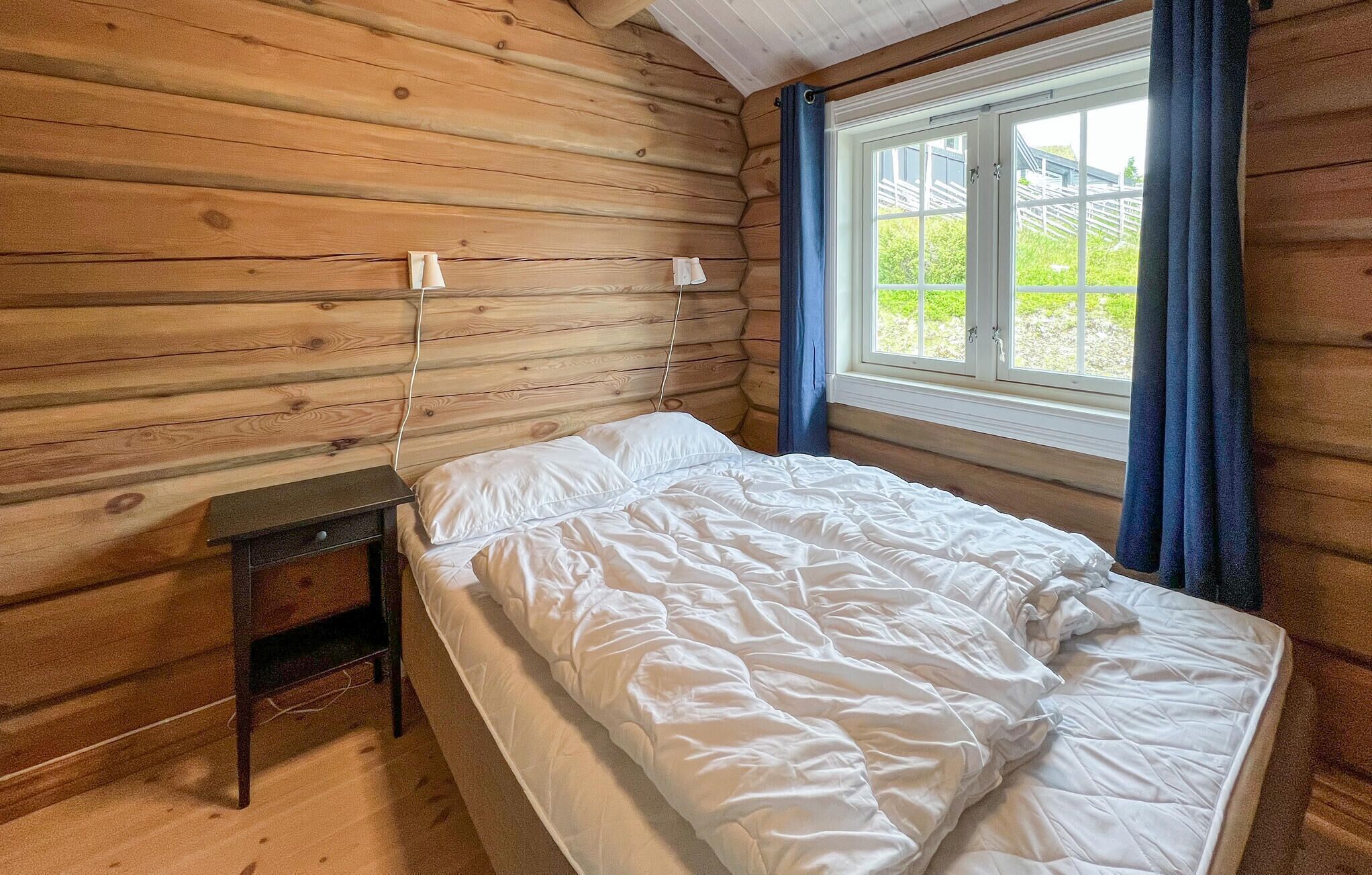 Une chambre dans un chalet en bois, avec un lit, une table de chevet et une fenêtre avec des rideaux.
