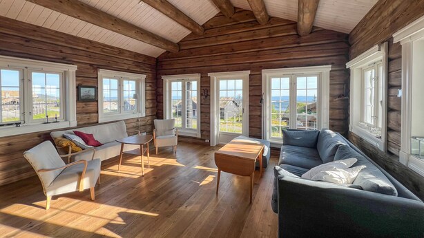 A cozy log cabin interior with a wooden ceiling, large windows, a sofa, chairs, and a small table. - Nice home in Sjusjøen with house a mountain view (Sjusjøen)