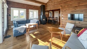 A cozy cabin interior with a wooden interior, a sofa, a dining table, and a TV mounted on the wall. - Nice home in Sjusjøen with house a mountain view (Sjusjøen)