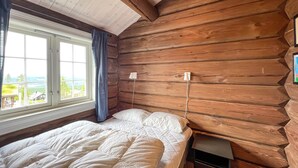 A log cabin room with a bed, a nightstand, and a window with curtains. - Nice home in Sjusjøen with house a mountain view (Sjusjøen)