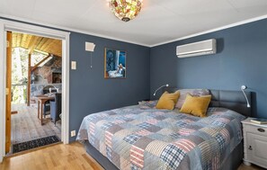 Quarto com uma cama grande, mesa de cabeceira, ar condicionado na parede e um quadro.