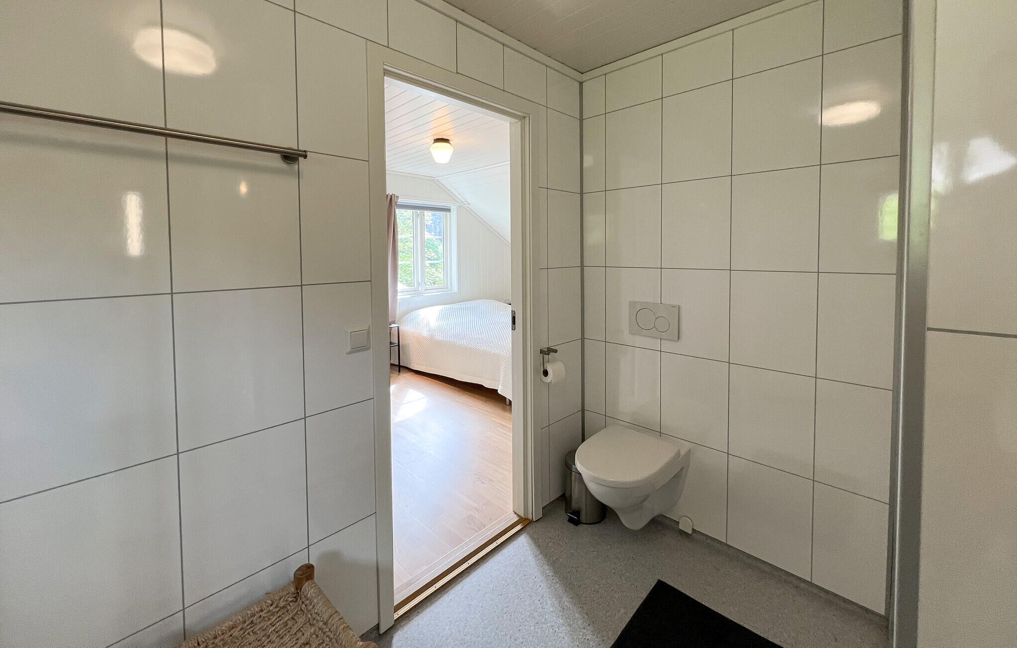 A small, modern bathroom with white tiles, a toilet, and a shower area.