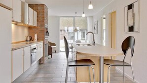 A modern kitchen with a central island, stainless steel appliances, and a brick accent wall. - 6 Person Holiday Home on a Holiday Park in Romo (Rømø)