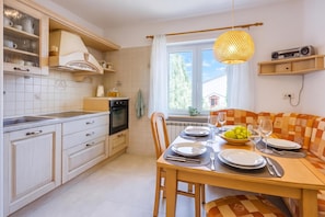 A modern kitchen with a dining area, featuring a wooden table set for two, a built-in oven, and a window with a view.