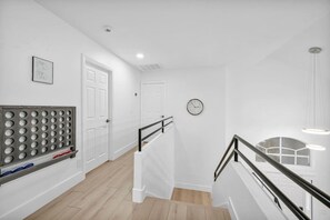 A modern, minimalist hallway with white walls, a wooden floor, and a metal railing.