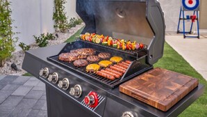 A barbecue grill with multiple cooking zones, a wooden cutting board, and a target in the background.