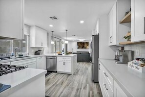 A modern kitchen with white cabinetry, a central island, a coffee bar, and a built-in oven.