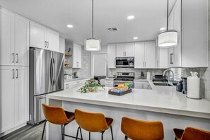 A modern kitchen with white cabinets, stainless steel appliances, and a central island with bar stools.