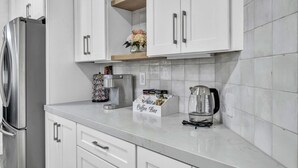 A kitchen with white cabinets, a stainless steel refrigerator, a coffee maker, and a coffee bar.