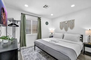 A modern hotel room with a large bed, a TV, a desk, and a window with curtains.