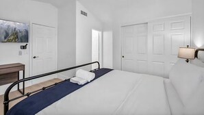 A hotel room with a bed, a desk, a chair, a ceiling fan, and a door.