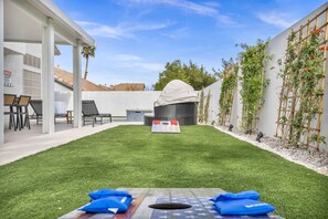 A backyard with a covered seating area, a grill, and a small table with cushions.