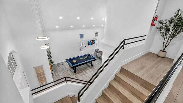 A modern interior with a pool table, staircase, and potted plants.