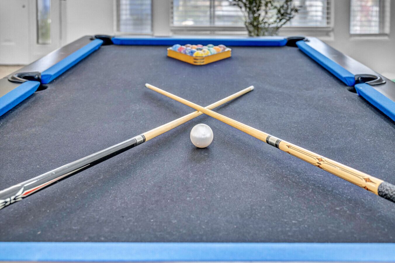 Ein Billardtisch mit zwei Queue-Stöcken, die über einem weißen Billardball kreuzen, und ein Satz Murmeln im Hintergrund.