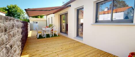 A wooden deck with a table and chairs, a covered patio area, and a large window.