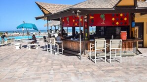 An outdoor bar area with a pool, lounge chairs, and a thatched-roof structure.