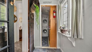 A laundry room with a washing machine, a fire extinguisher, and a shelf with decorative items. - Adorable Seaside Cottage (Old Orchard Beach)
