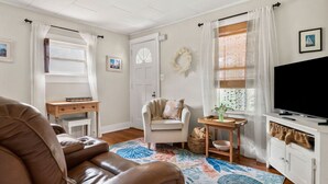A cozy living room with a leather sofa, a white armchair, a small wooden table with a vase, and a TV on a white cabinet. - Adorable Seaside Cottage (Old Orchard Beach)