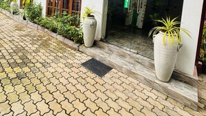 A building entrance with a tiled pathway leading up to it, large potted plants, and a glass door. - Green Path  (Gampaha)
