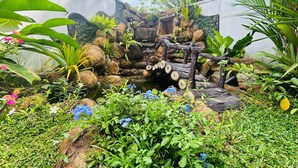 A garden with a rock waterfall, lush greenery, and flowering plants. - Green Path  (Gampaha)