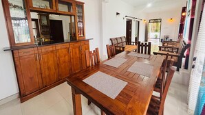 A dining area with a wooden table and chairs, a cabinet with glass doors, and a staircase leading to an upper level. - Green Path  (Gampaha)