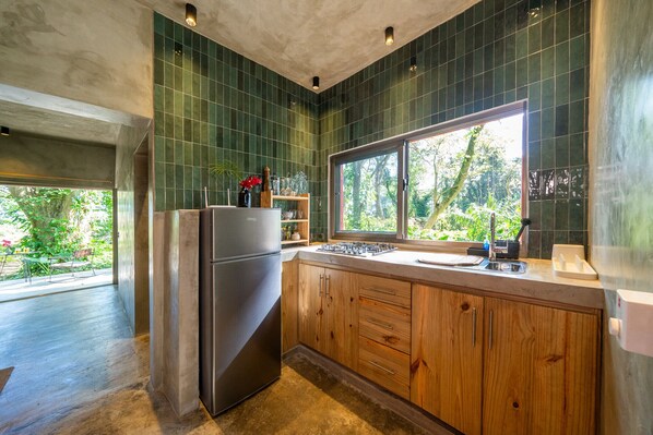 A modern kitchen with green tiles, wooden cabinets, a stainless steel refrigerator, and a window overlooking greenery. - REFUGIO Sabaneta de Yásica (Sosua)