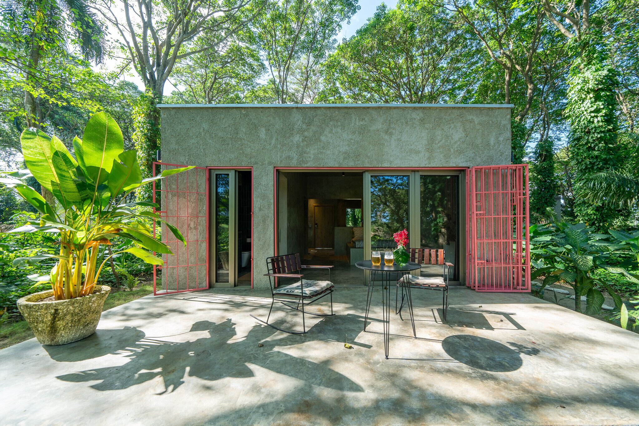 Uma casa moderna com fachada de concreto, grandes janelas e um espaço de varanda com mesa e cadeiras.