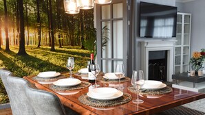 Une table à manger dressée avec des assiettes, des verres et une bouteille, avec une télévision et une cheminée en arrière-plan.