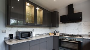 Une cuisine moderne avec des meubles de couleur sombre, un four à micro-ondes encastré, une cuisinière à gaz et un dosseret en marbre.