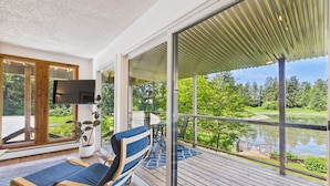 A modern room with a large sliding glass door leading to a deck overlooking a lake. - Hi Tide Retreat w/ Bayfront Deck & Ocean Views (Juneau)