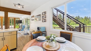 A modern kitchen with wooden cabinets, a dining table set with white plates, and a view of a wooden deck and staircase. - Hi Tide Retreat w/ Bayfront Deck & Ocean Views (Juneau)