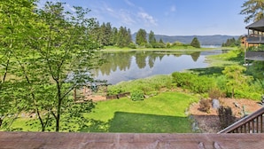 A lakeside view with a wooden deck, lush greenery, and a distant mountain range. - Hi Tide Retreat w/ Bayfront Deck & Ocean Views (Juneau)