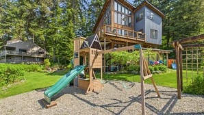 A two-story wooden house with a balcony, a swing set, and a slide in the backyard. - Waterfront 5-Bedroom Retreat w/ Sauna & Firepit (Juneau)