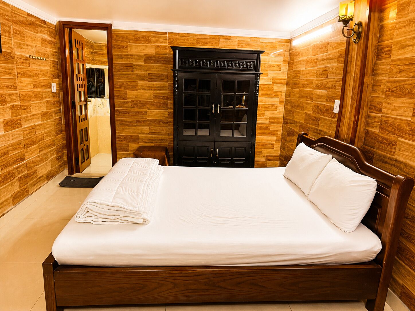 Ett hotellrum med en väggpanel av trä, en säng med vita sängkläder och en svart garderob med glasdörrar.