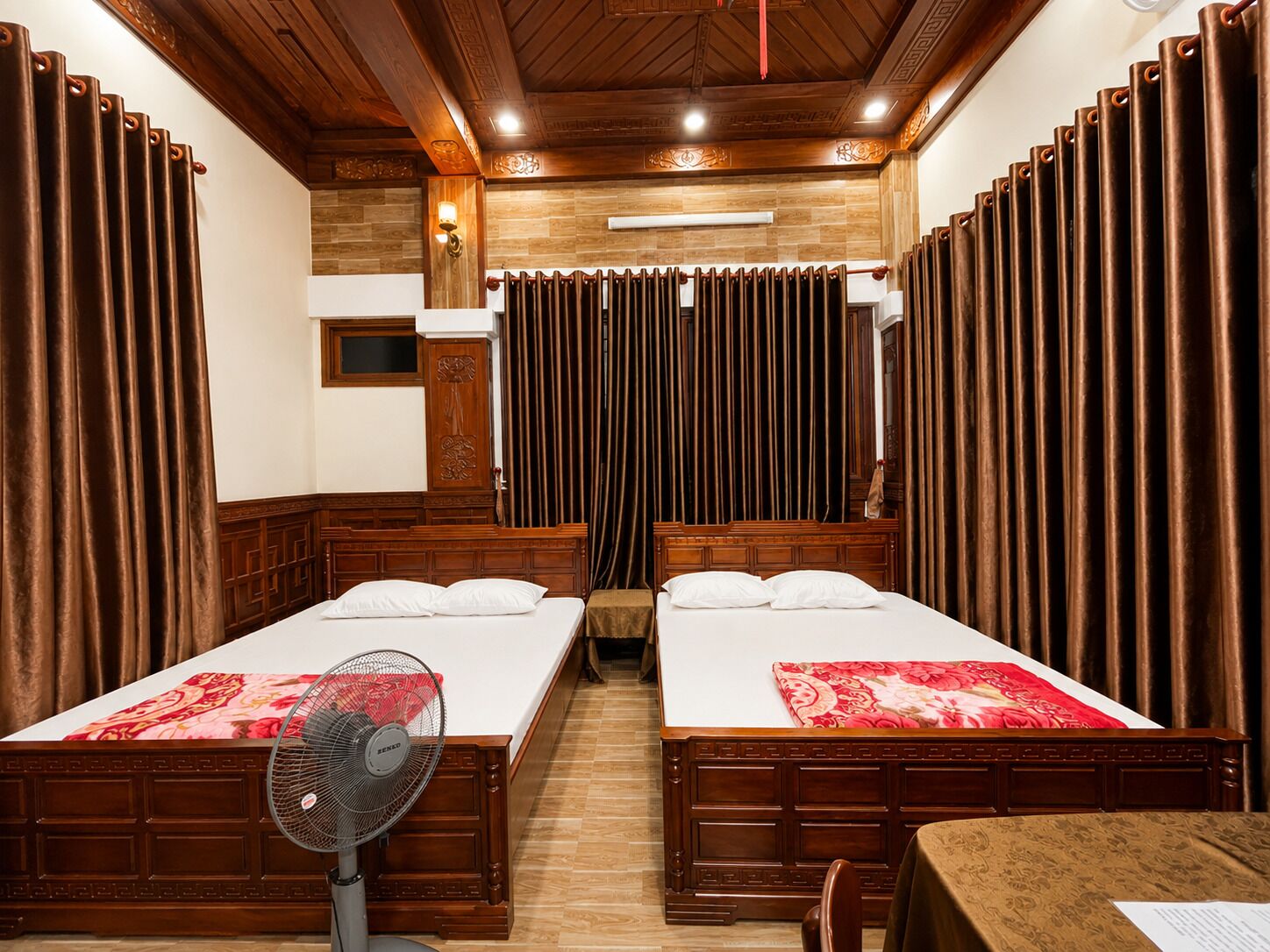A hotel room with two beds, a wooden ceiling, a fan, and curtains.