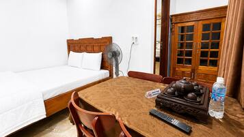Habitación de hotel con cama, una mesa con sillas, un ventilador, una tetera, un control remoto y una botella de agua.