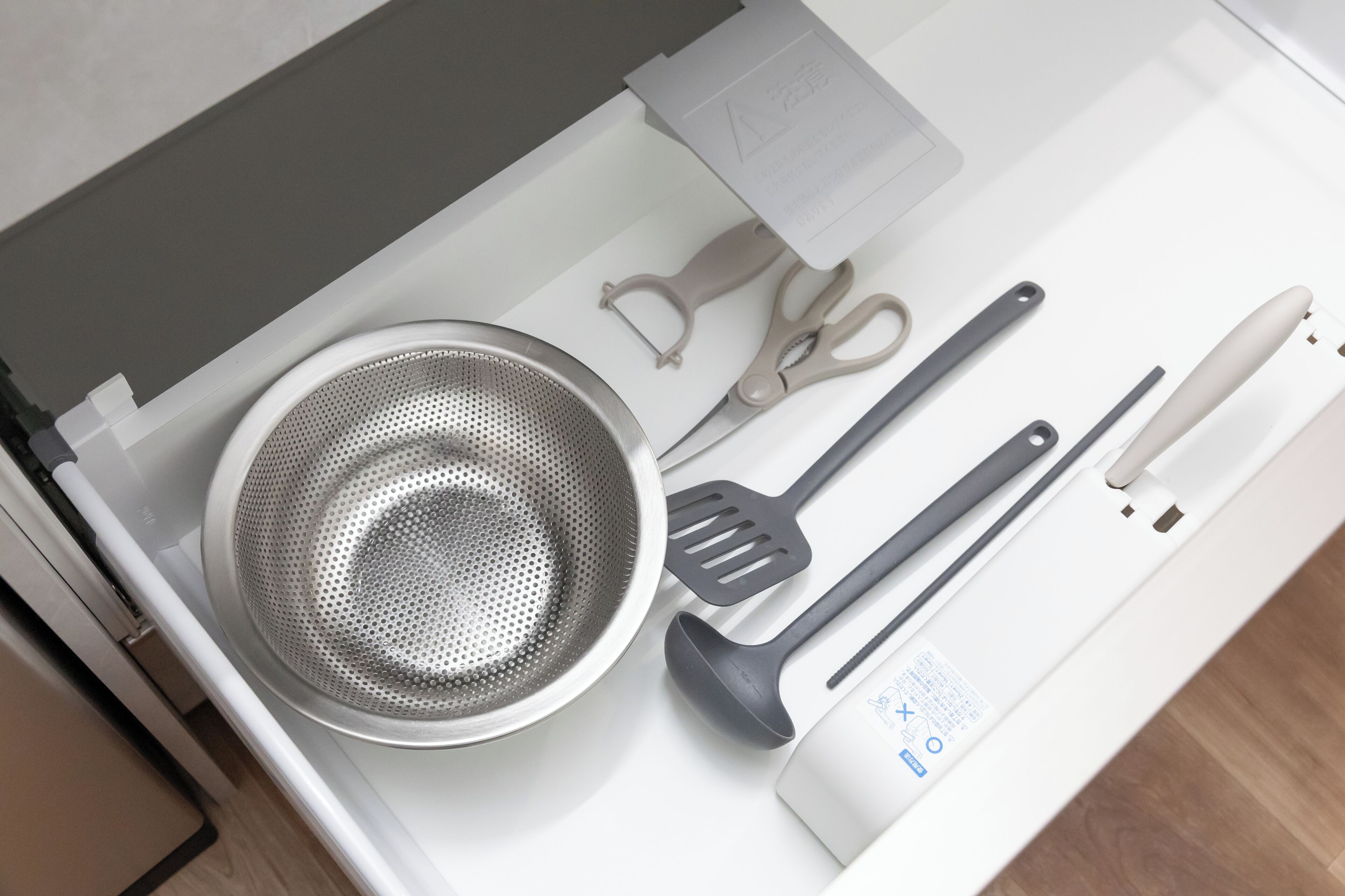 A kitchen with a stainless steel colander, a pair of scissors, a spatula, and a white appliance on the counter.