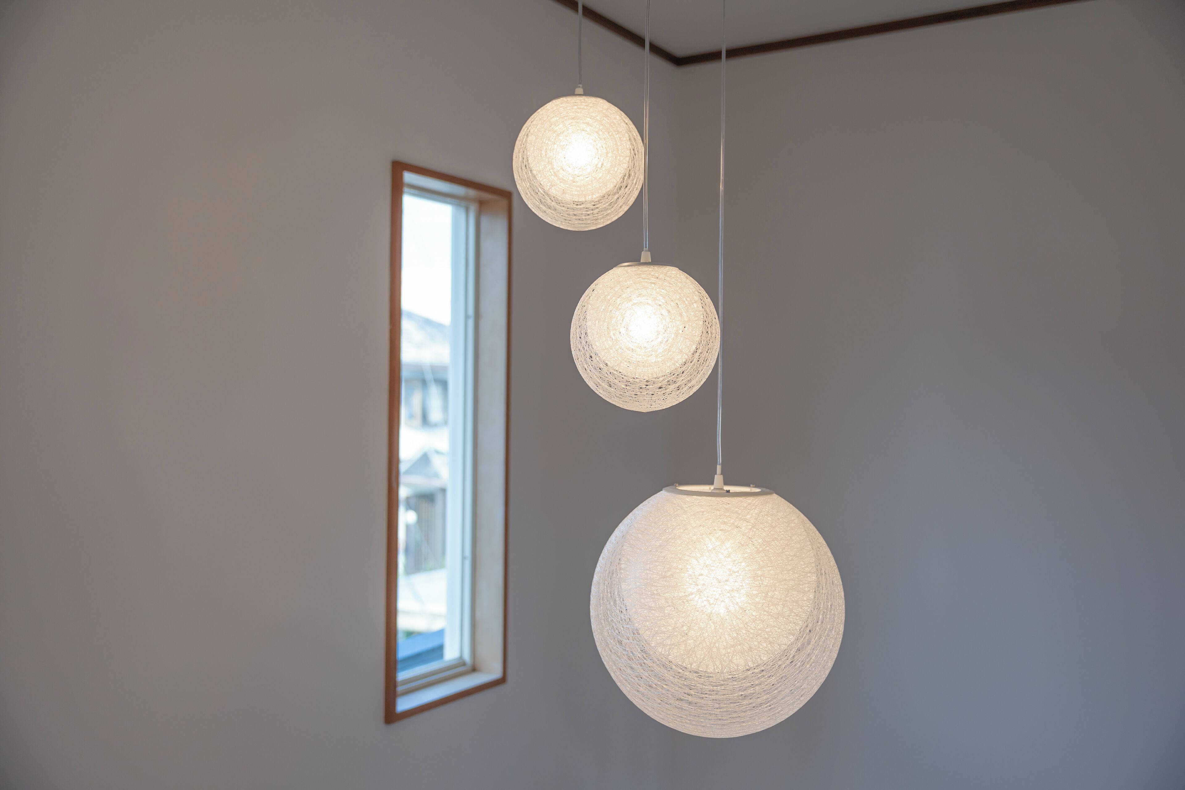 A room with a large window, three spherical hanging lights, and a framed picture on the wall.