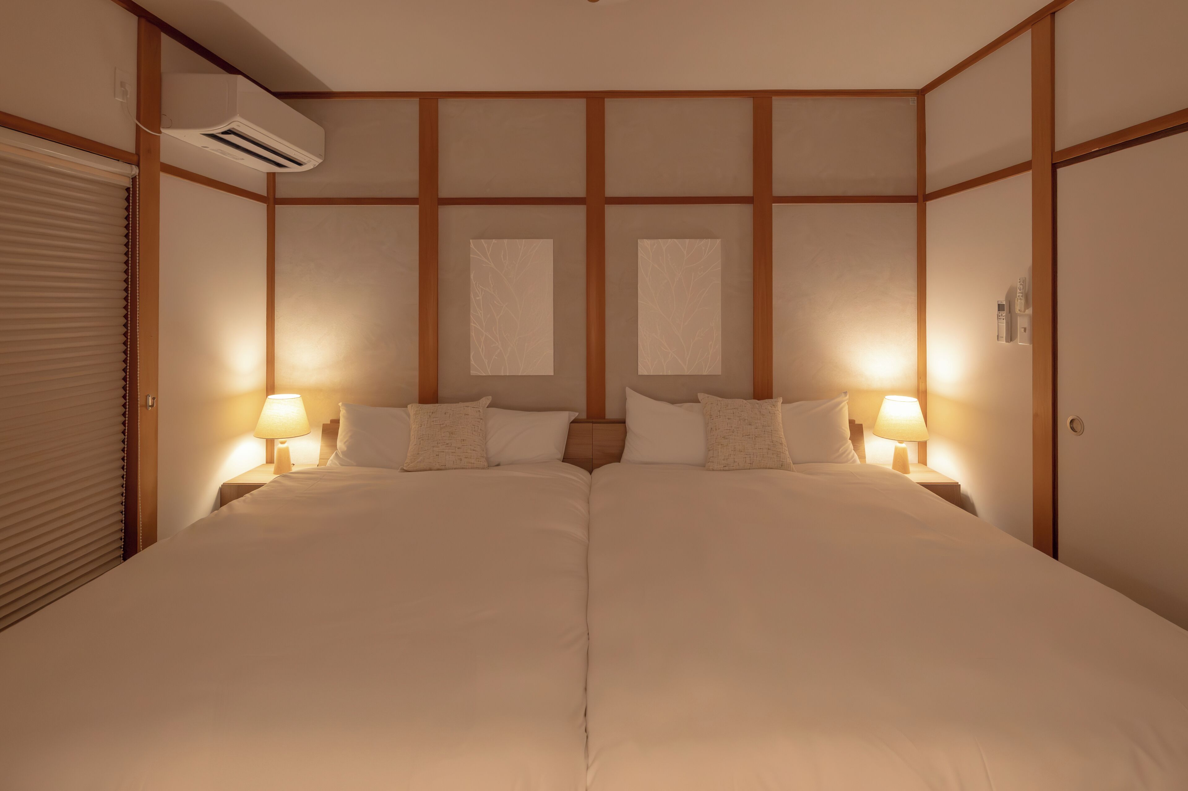 Una habitación de hotel con una cama grande, dos lámparas de noche, un ventanal con vistas y un equipo de aire acondicionado.