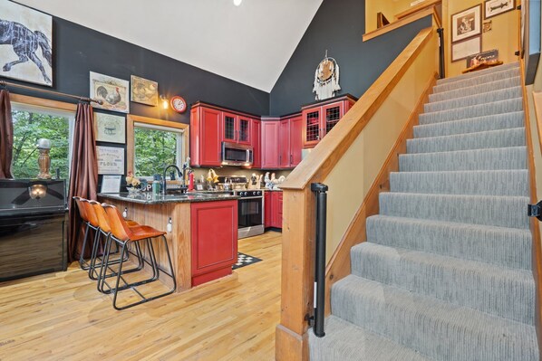 A kitchen with red cabinets, a wooden staircase, and a view of trees outside.
